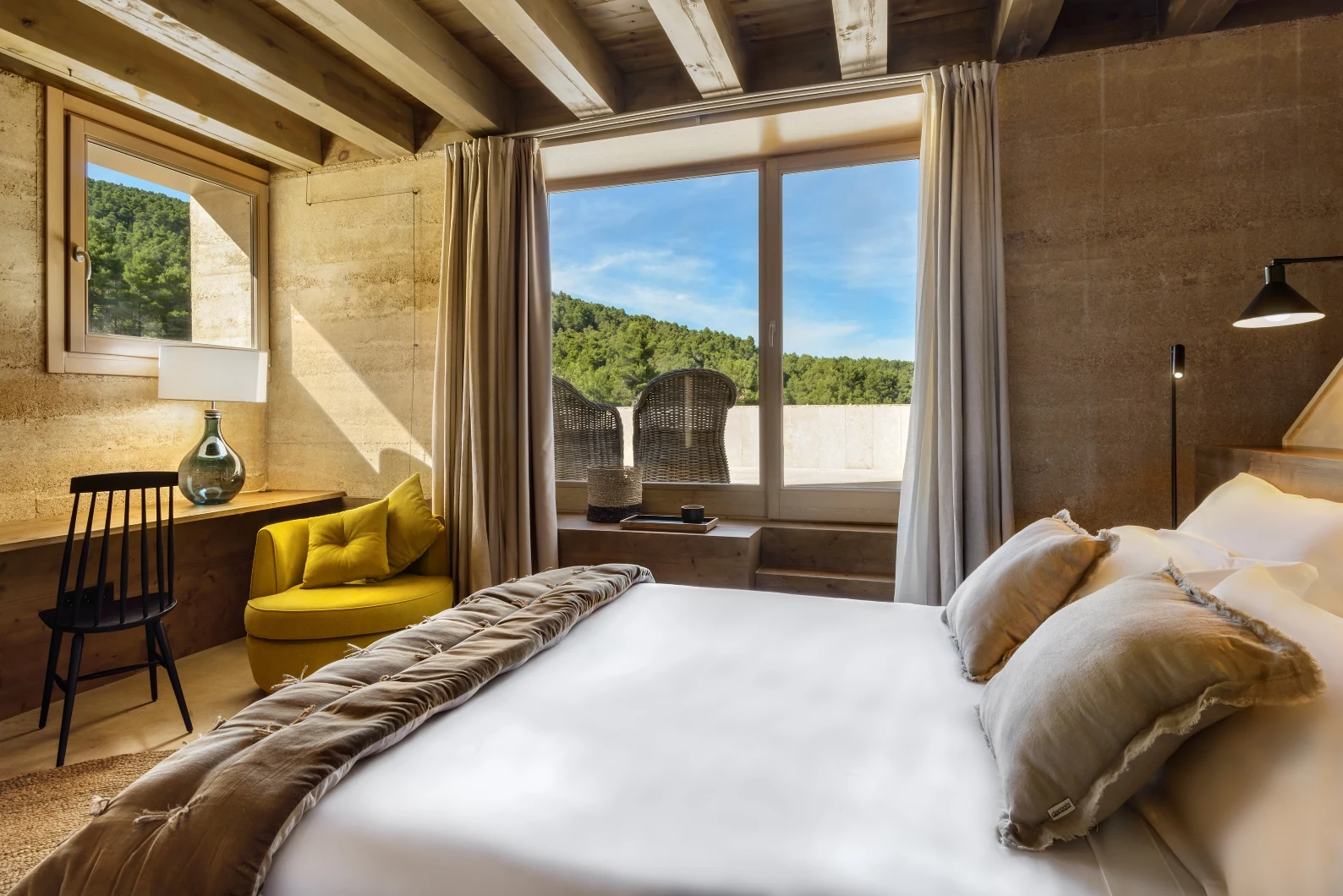 SLH_Hotel_Torre_del_Marques_habitacion_Bacana_Communications Habitación de Torre del Marqués con cama, zona de lectura y vistas al paisaje natural desde la terraza.