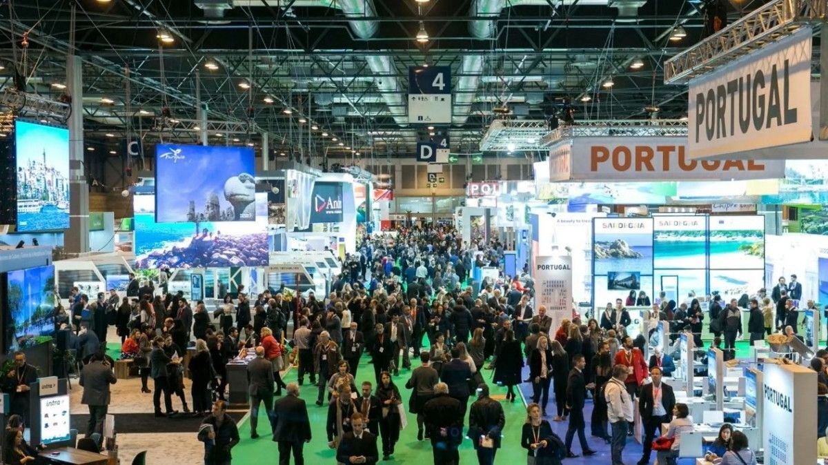 Visitantes recorren un pabellón de una feria internacional de turismo con los stands de Portugal y Cerdeña