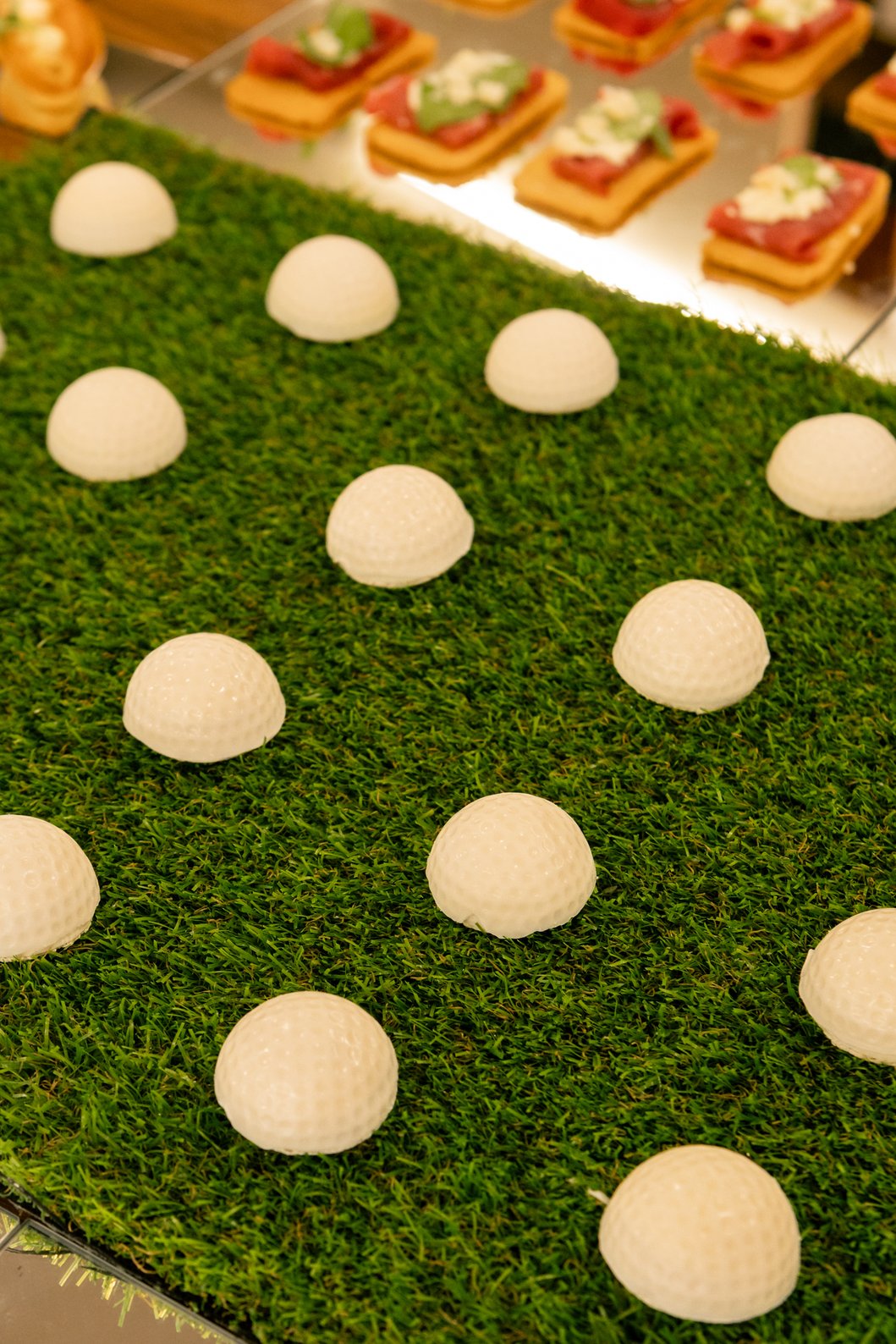 Piezas blancas con forma de bola de golf sobre una base de césped, junto a canapés